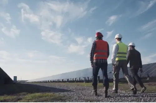 Three men walking along solar panels - Energy Image